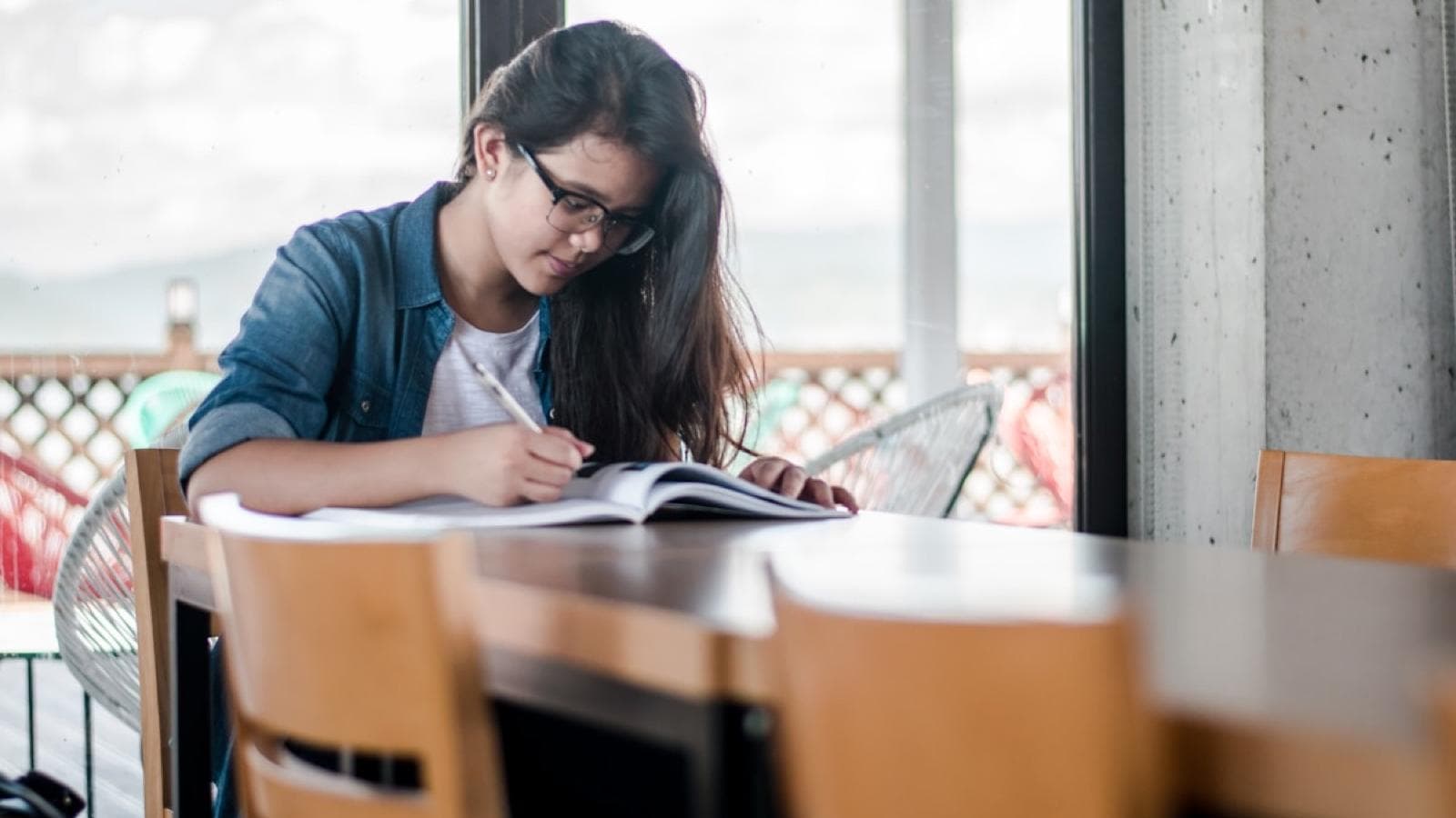A student writing notes from a textbook at a study table