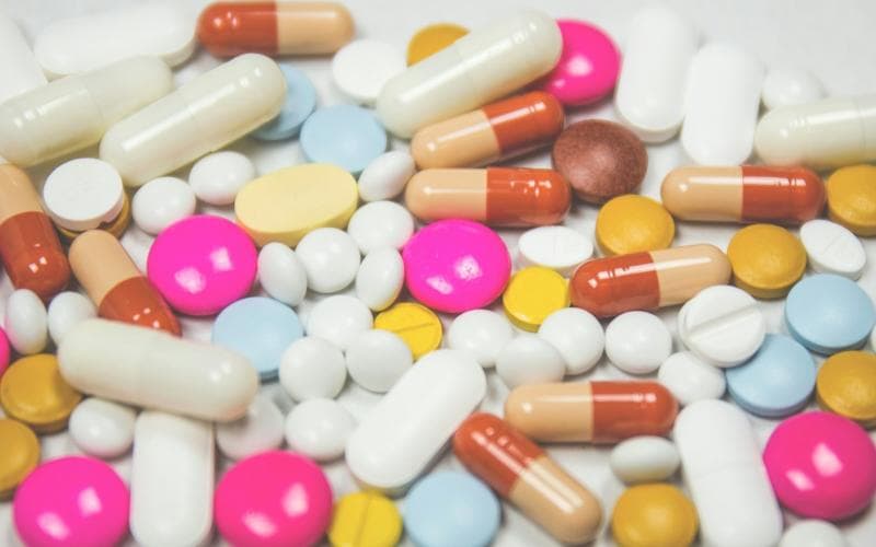 Assorted tablets and capsules of different colours on a white surface