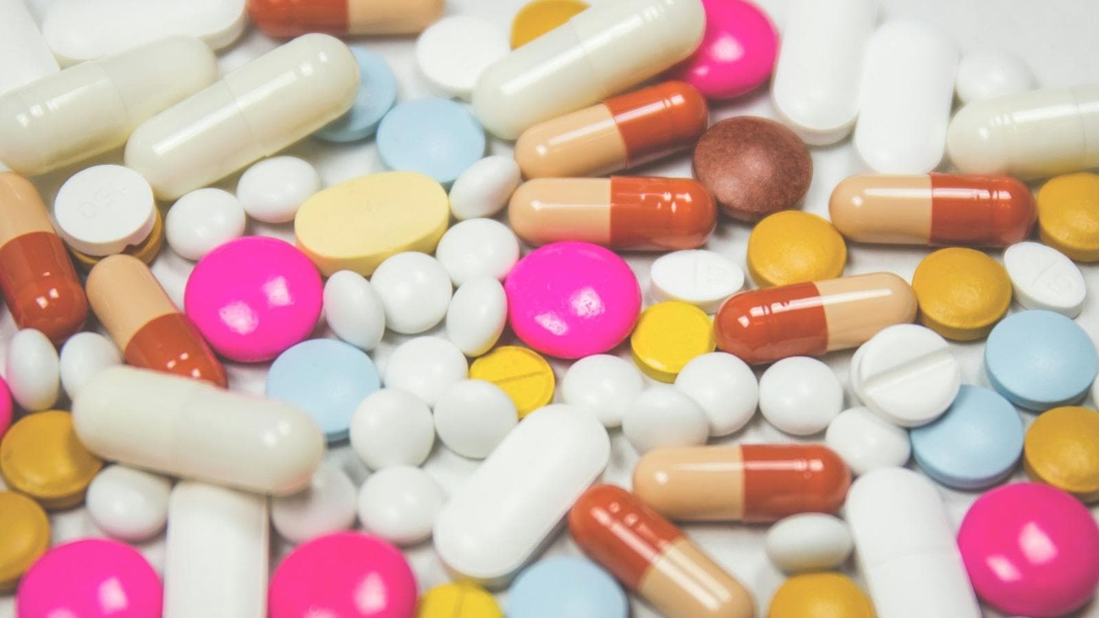 Assorted tablets and capsules of different colours on a white surface