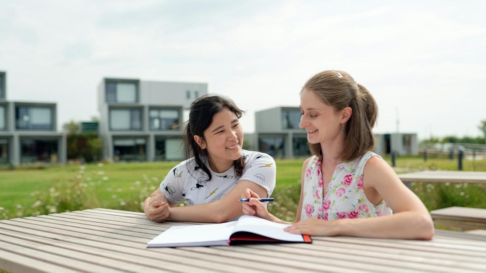 Two nursing students revising together from a notebook on a campus bench